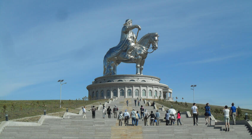 Chinggis Khaan Equestrian Statue Complex with tourists on the steps against a blue sky.