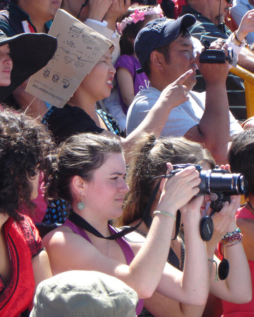 A tourist taking photos with a camera in a crowd of spectators at Mongolia's Three
                        Manly Games festival stadium.