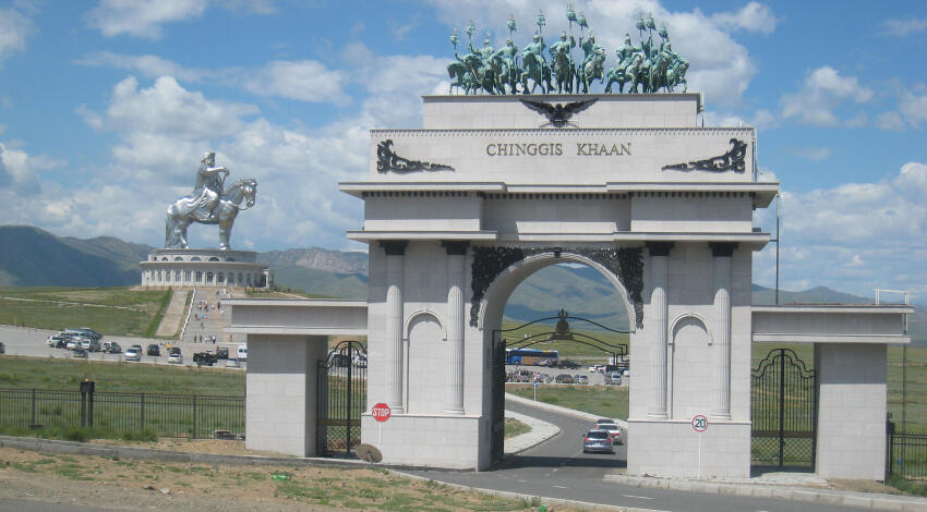 Chinggis Khaan Statue Complex entrance gate topped with bronze horsemen, statue on the hill beyond.