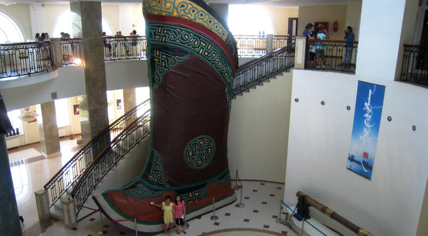 Two visitors dwarfed by the 9m Mongolian gutal boot, with the giant golden whip displayed beside it.