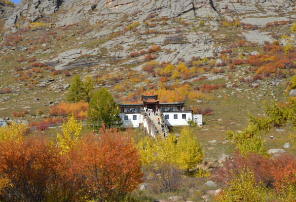 White Buddhist temple on a rocky hillside among red and yellow autumn bushes in Terelj National Park