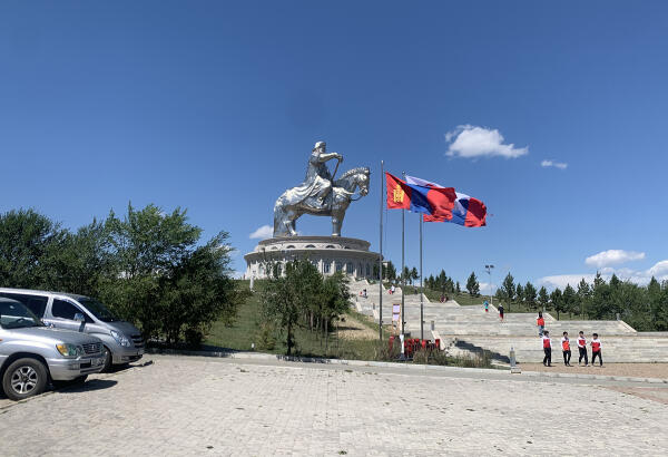 Chinggis Khaan's silver equestrian statue towering over its complex, with Mongolian flags and tourists below.