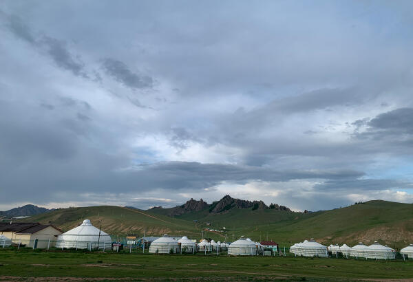 Rows of white gers at a tourist camp in Terelj National Park, with green hills and rocky peaks behind.