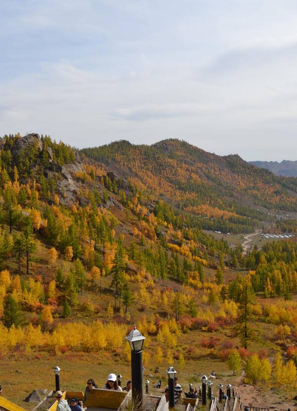 Autumn landscape of Terelj National Park viewed from Ariyabal Temple, with golden trees, hills, and visitors.