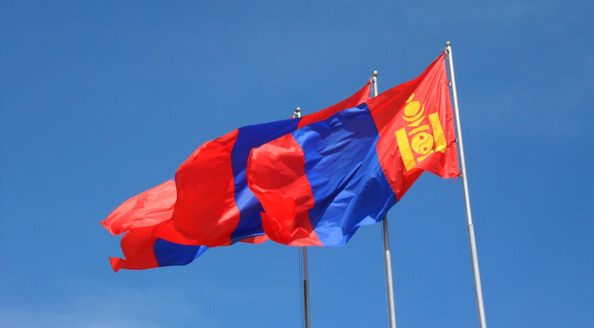 Three Mongolian national flags flying on tall flagpoles against a clear blue sky.